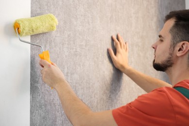 Man hanging stylish gray wallpaper in room