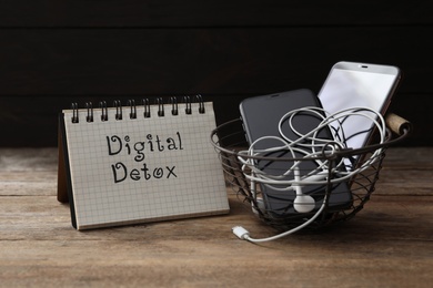 Photo of Trash bin with different gadgets and words DIGITAL DETOX on wooden table