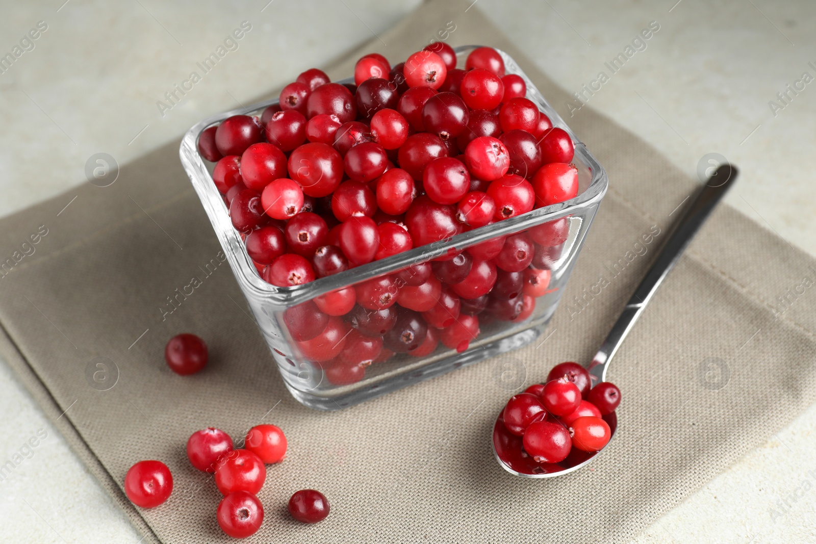 Photo of Cranberries in bowl and spoon on light grey table, closeup