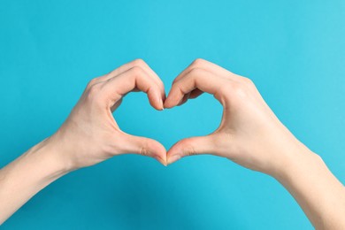 Woman showing heart gesture with hands on light blue background, closeup