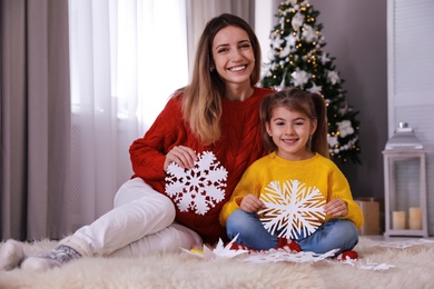 Photo of Happy mother and daughter with paper snowflakes near Christmas tree at home
