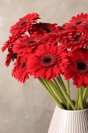 Photo of Bouquet of beautiful red gerbera flowers in ceramic vase on beige background, closeup