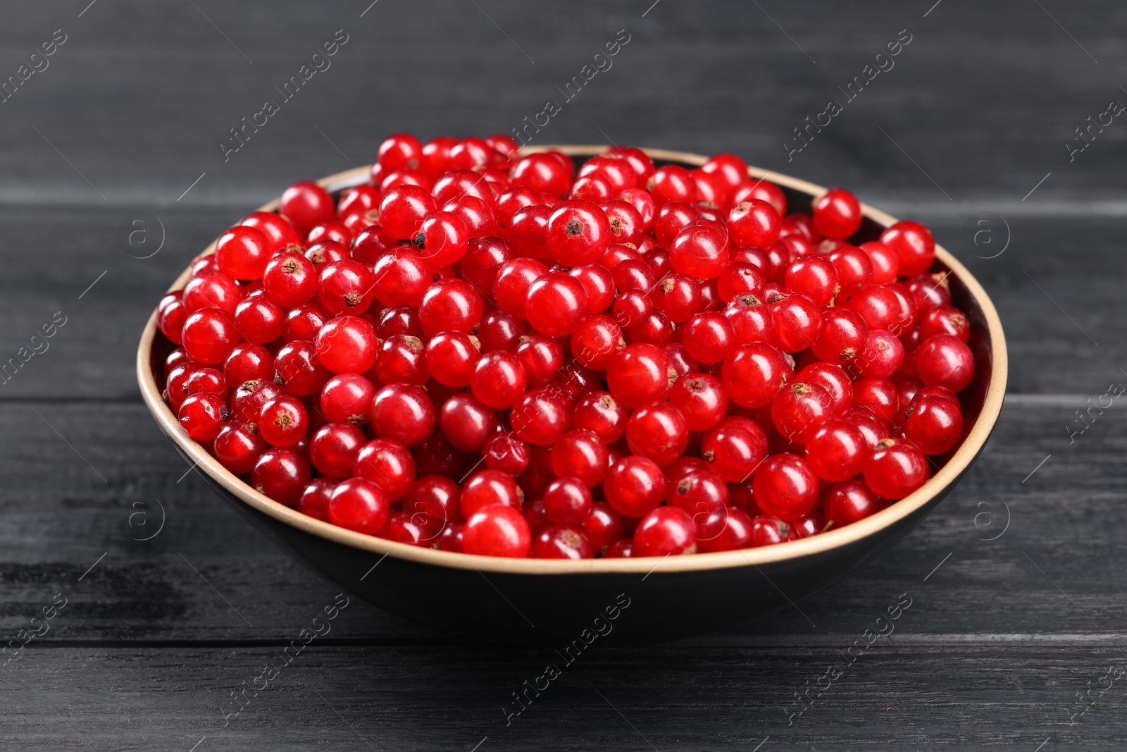 Photo of Ripe red currants in bowl on wooden rustic table