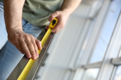 Photo of Man measuring metal railing, closeup view with space for text. Construction tool