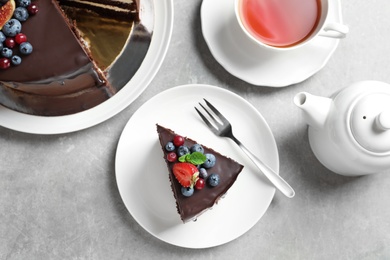 Photo of Delicious chocolate sponge berry cake and tea set on grey background, top view