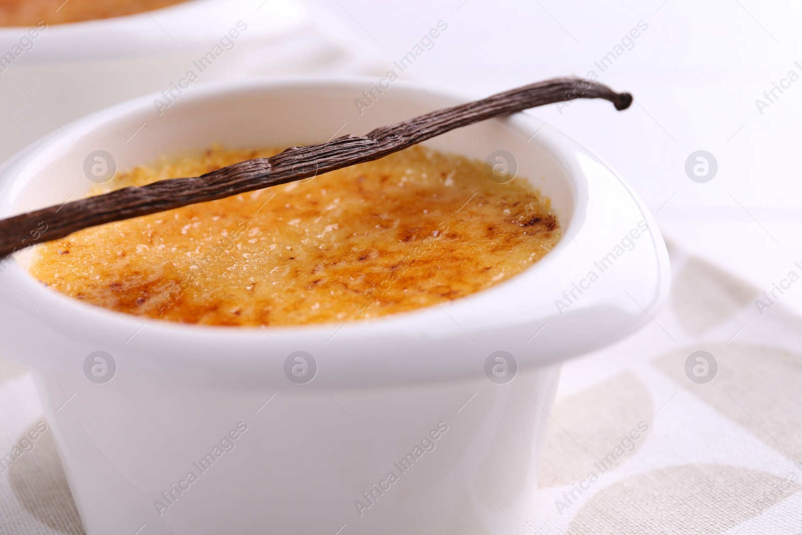 Photo of Delicious creme brulee in bowl and vanilla pod on table, closeup