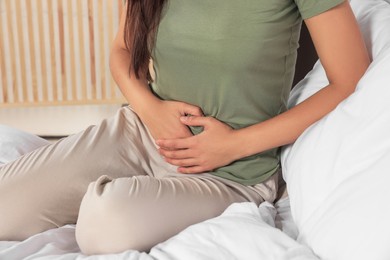 Photo of Young woman suffering from cystitis on bed indoors, closeup