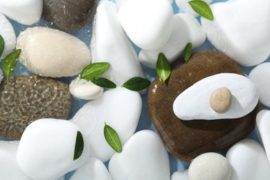 Spa stones and green leaves in water on light blue background, flat lay