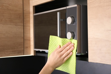 Woman cleaning microwave oven with rag in kitchen, closeup