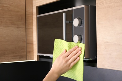 Photo of Woman cleaning microwave oven with rag in kitchen, closeup