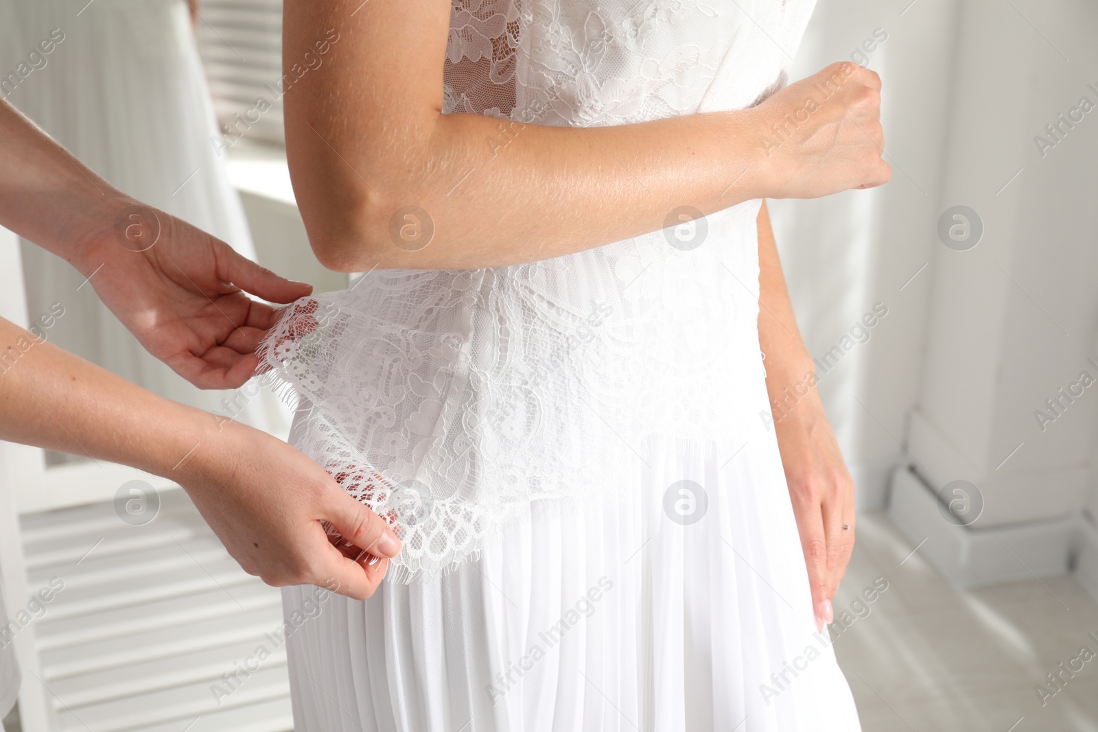 Photo of Woman helping bride to put on wedding dress indoors, closeup