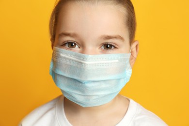Photo of Cute little girl in protective mask on yellow background