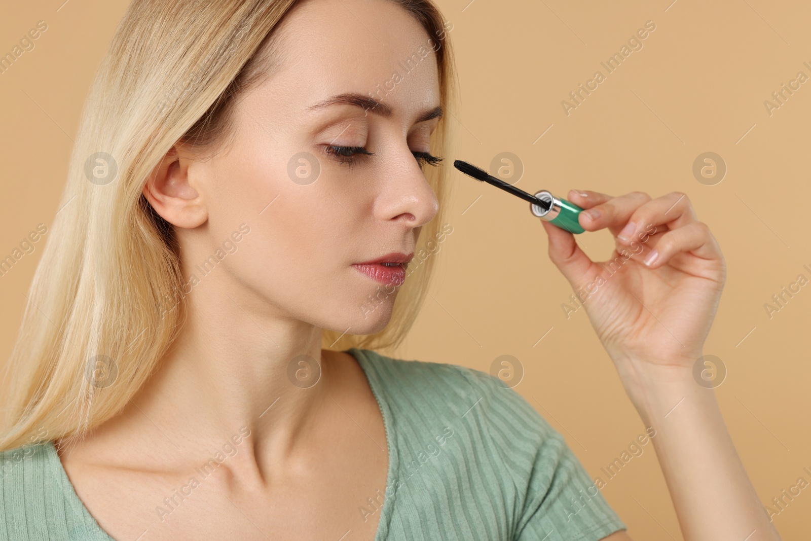 Photo of Beautiful woman applying mascara on beige background, closeup