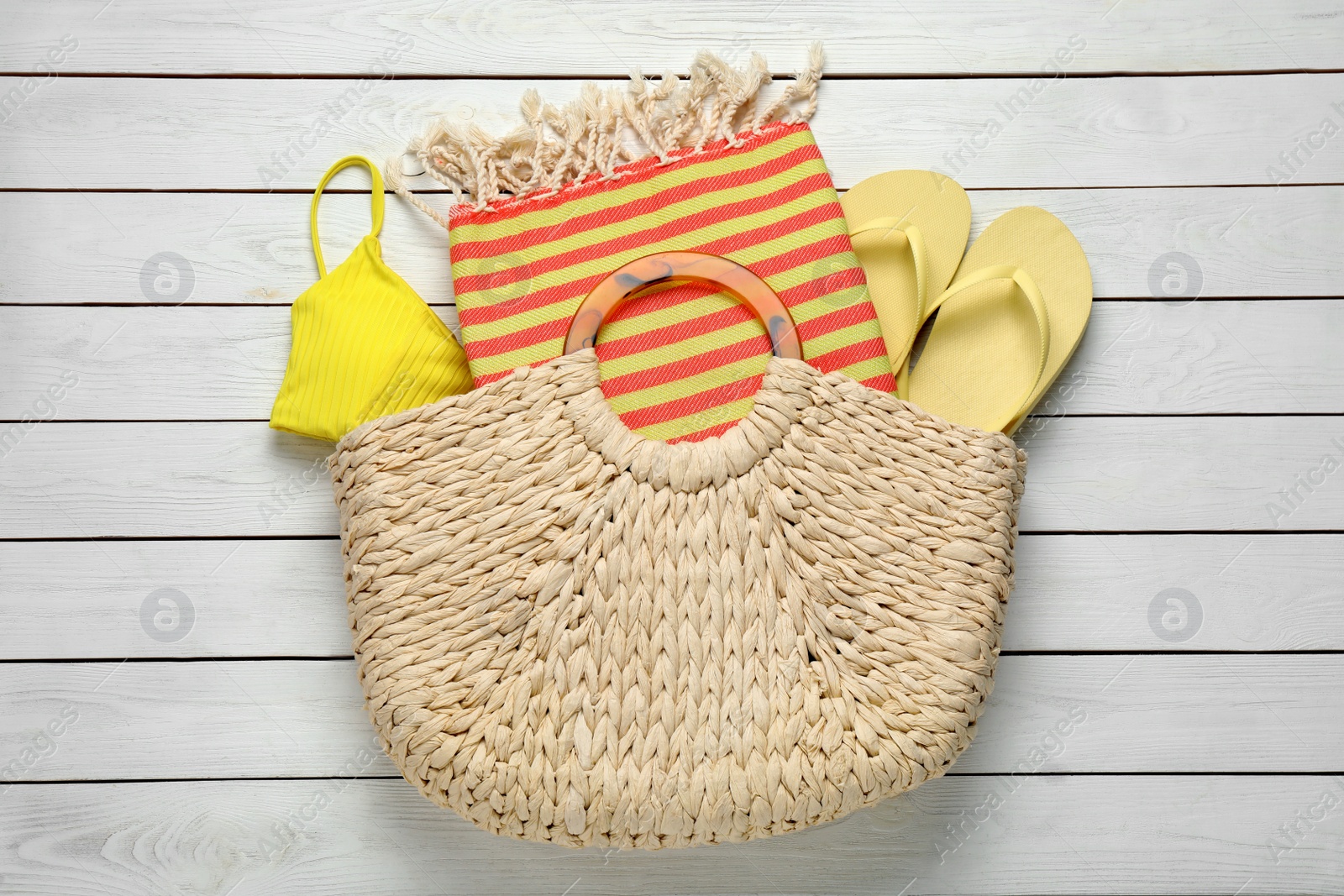 Photo of Beach bag with towel, flip flops and swimsuit on white wooden background, top view
