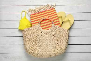 Photo of Beach bag with towel, flip flops and swimsuit on white wooden background, top view