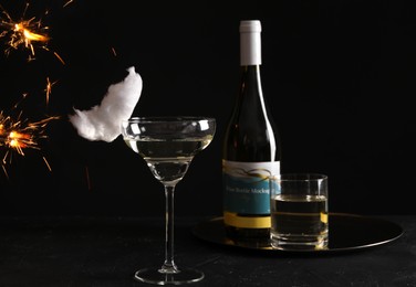 Photo of Cocktail with tasty cotton candy and bottle of alcohol drink on dark textured table