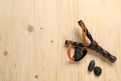 Black slingshot with stones on wooden table, flat lay. Space for text