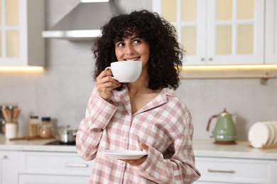 Photo of Beautiful young woman in stylish pyjama with cup of drink in kitchen