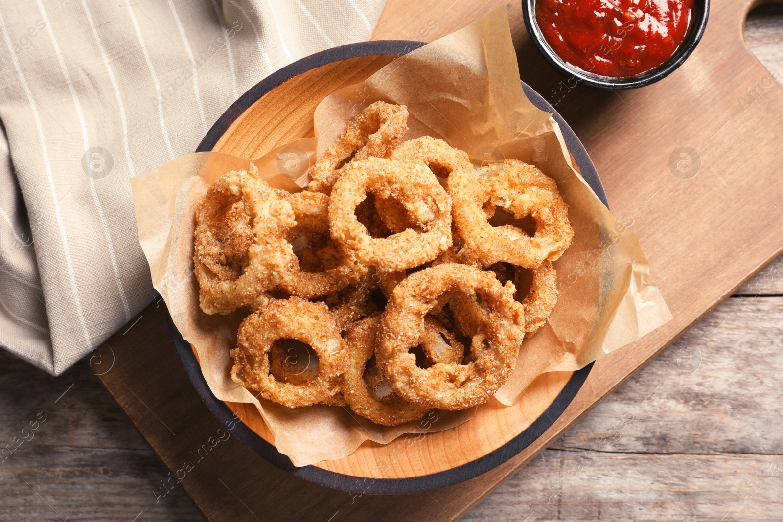Photo of Homemade crunchy fried onion rings in plate and sauce on wooden background, top view