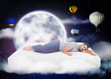Image of Sweet dreams. Dark cloudy sky with full moon and hot air balloons around sleeping young man 
