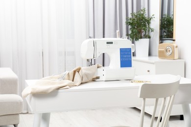 Photo of Sewing machine, measuring tape, scissors and fabric on white desk in workshop