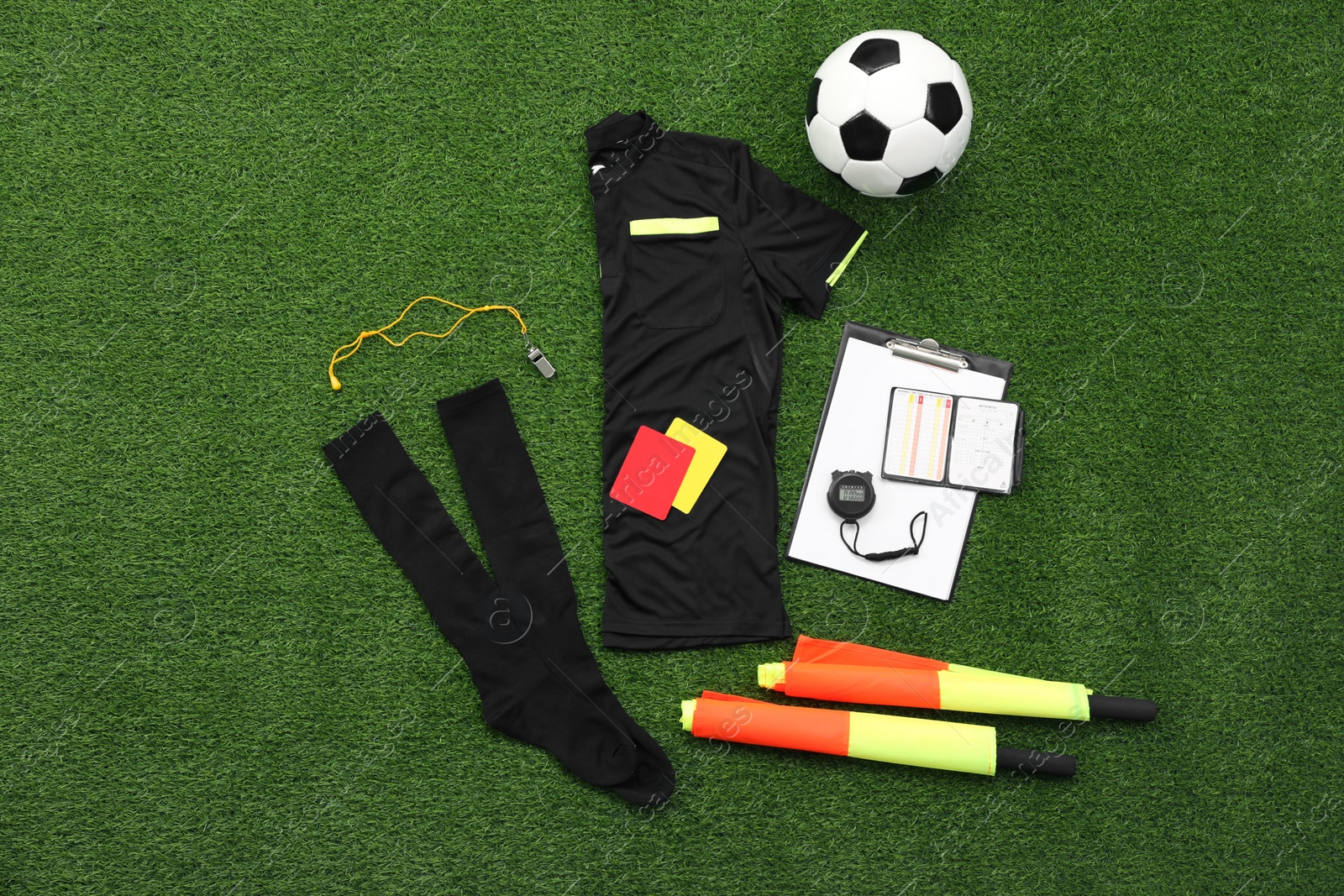 Photo of Uniform, soccer ball and other referee equipment on green grass, flat lay