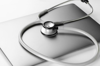 Photo of Modern laptop and stethoscope on white table, closeup