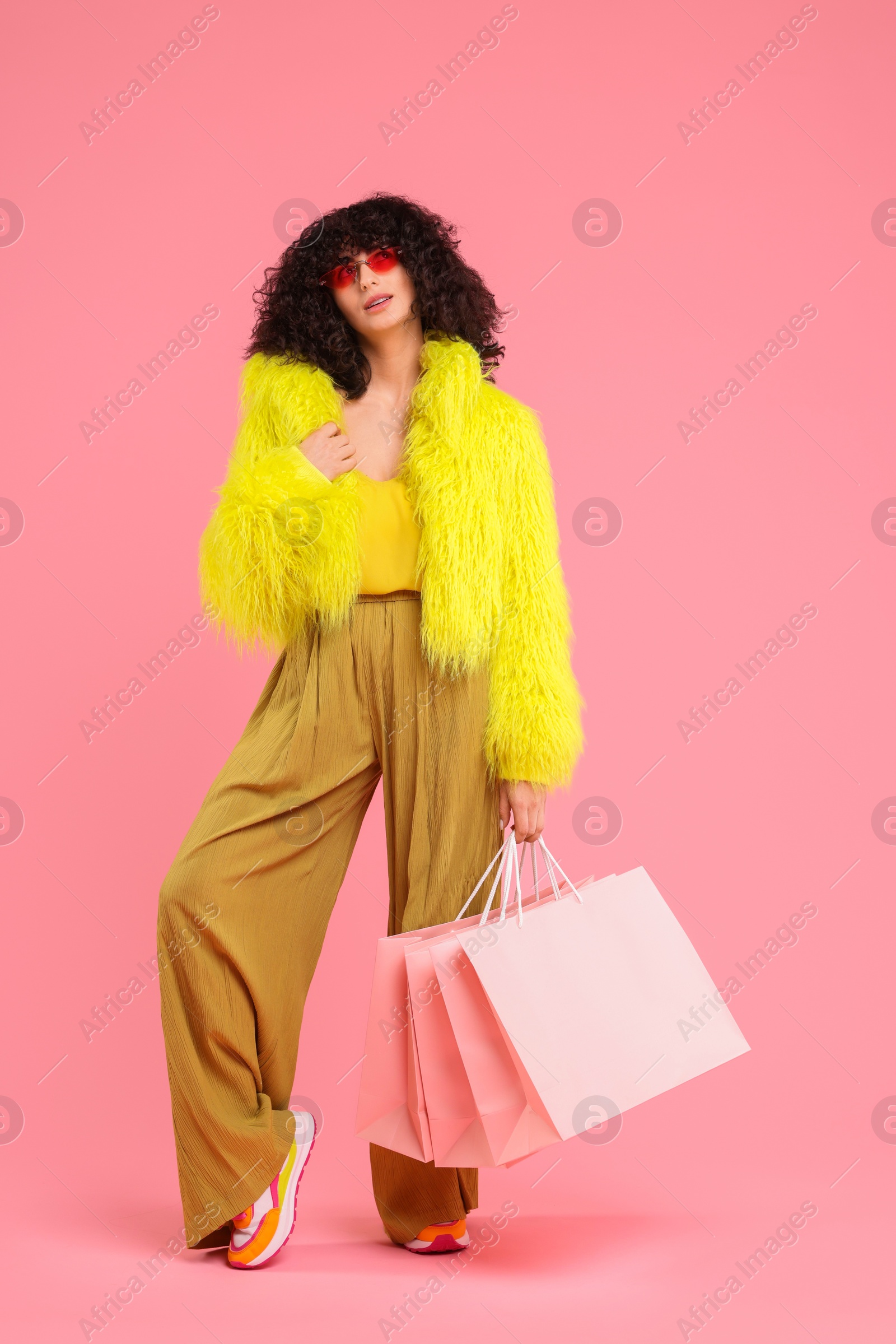 Photo of Happy young woman with shopping bags on pink background