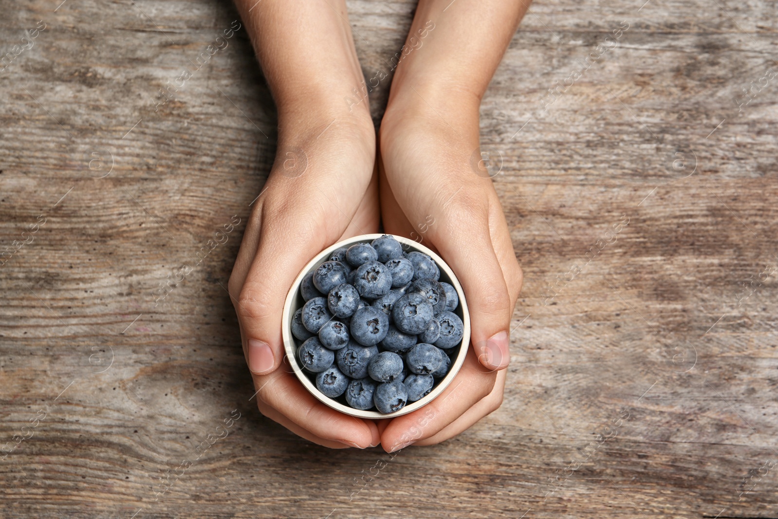 Photo of Woman holding juicy fresh blueberries on wooden table, top view