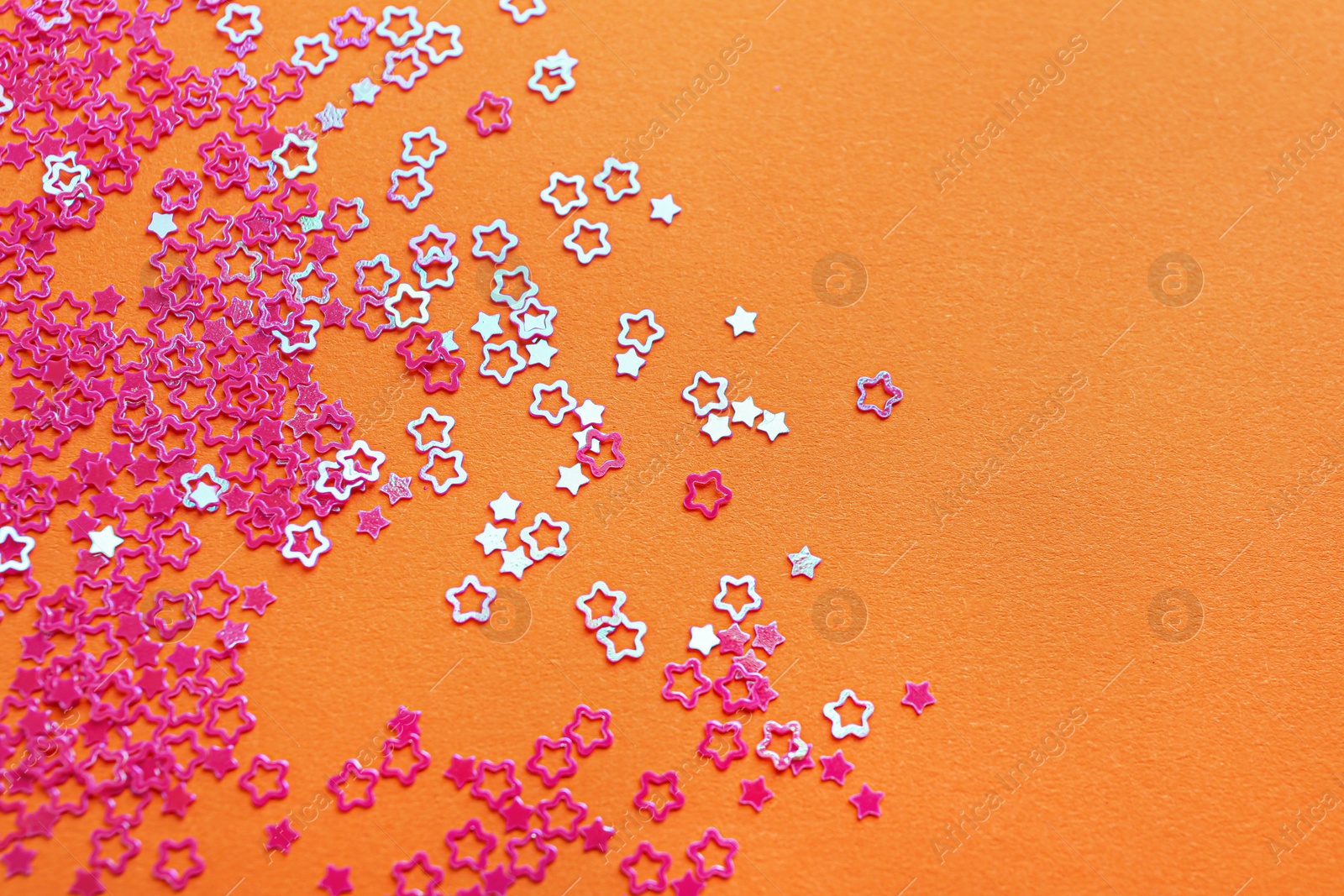 Photo of Shiny bright star shaped glitter on orange background. Space for text