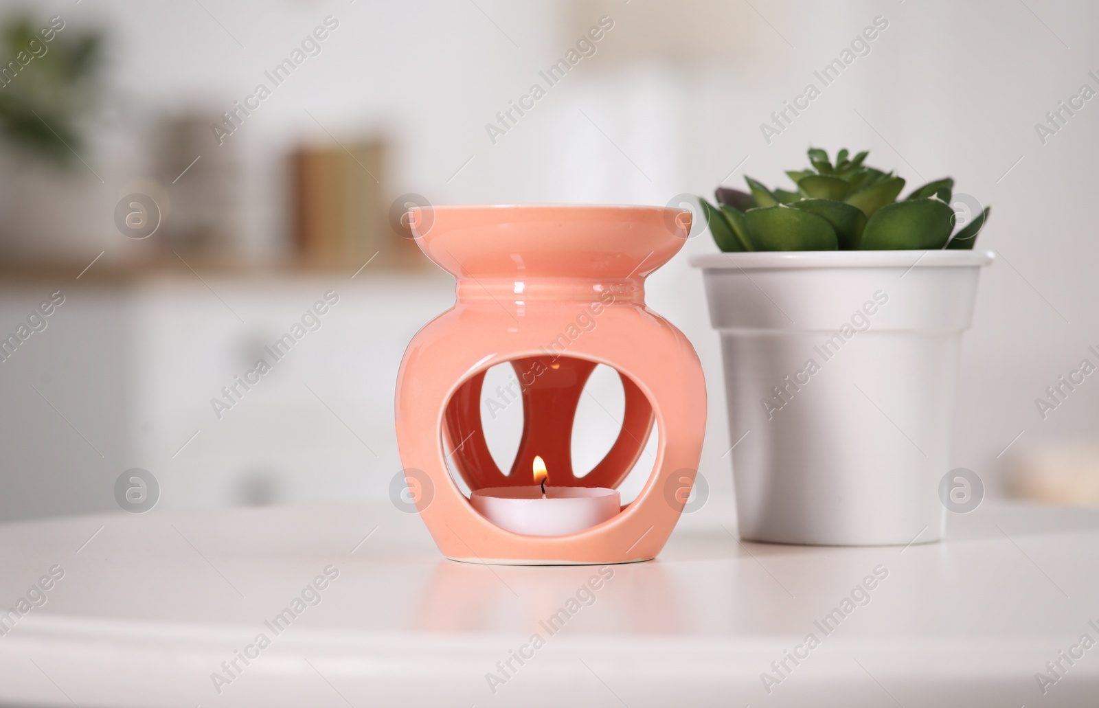 Photo of Stylish aroma lamp with small candle near houseplant on white table in room