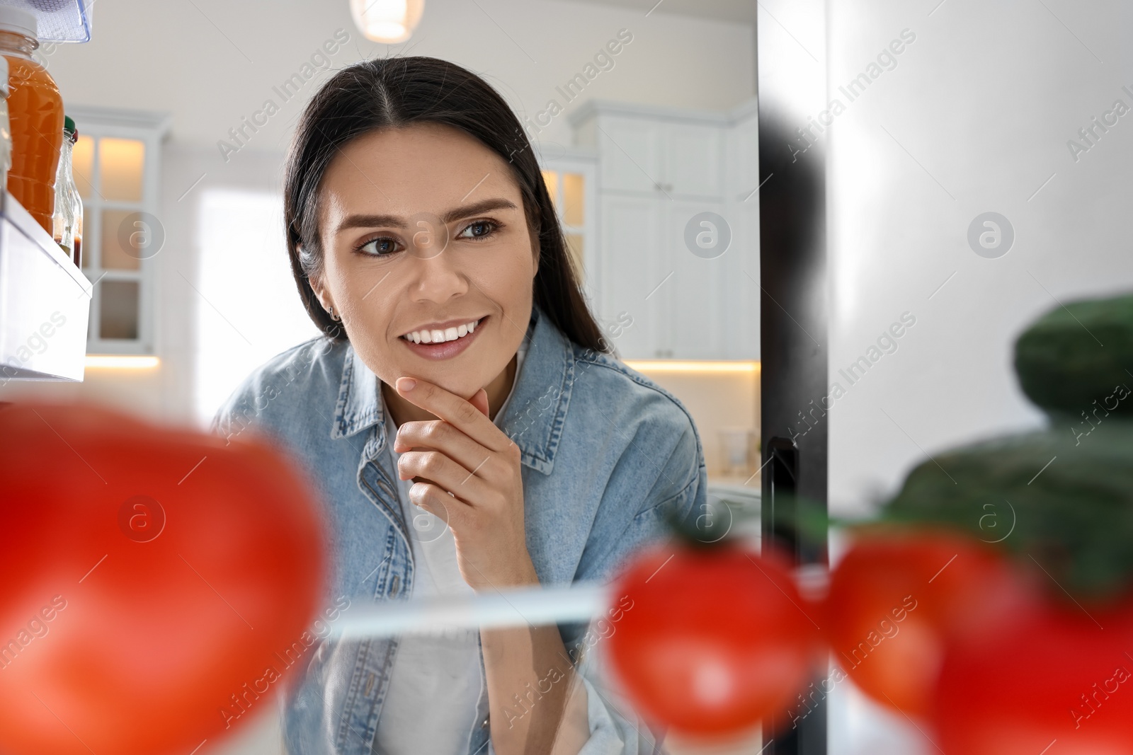 Photo of Thoughtful woman near refrigerator in kitchen, view from inside