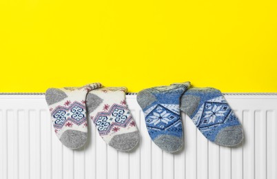 Photo of Knitted socks on heating radiator near yellow wall