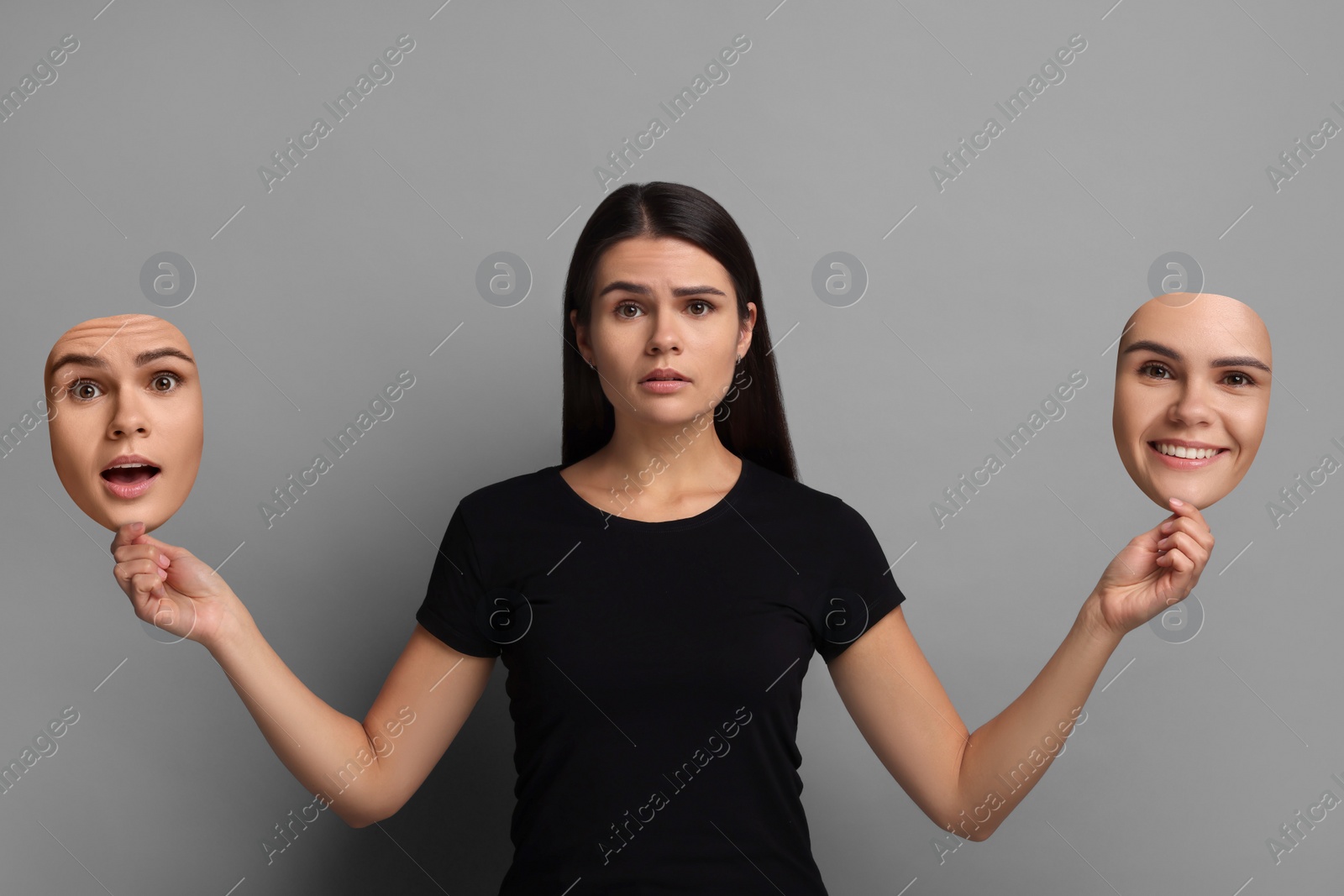 Image of Woman holding masks with her face showing different emotions on grey background. Balanced personality