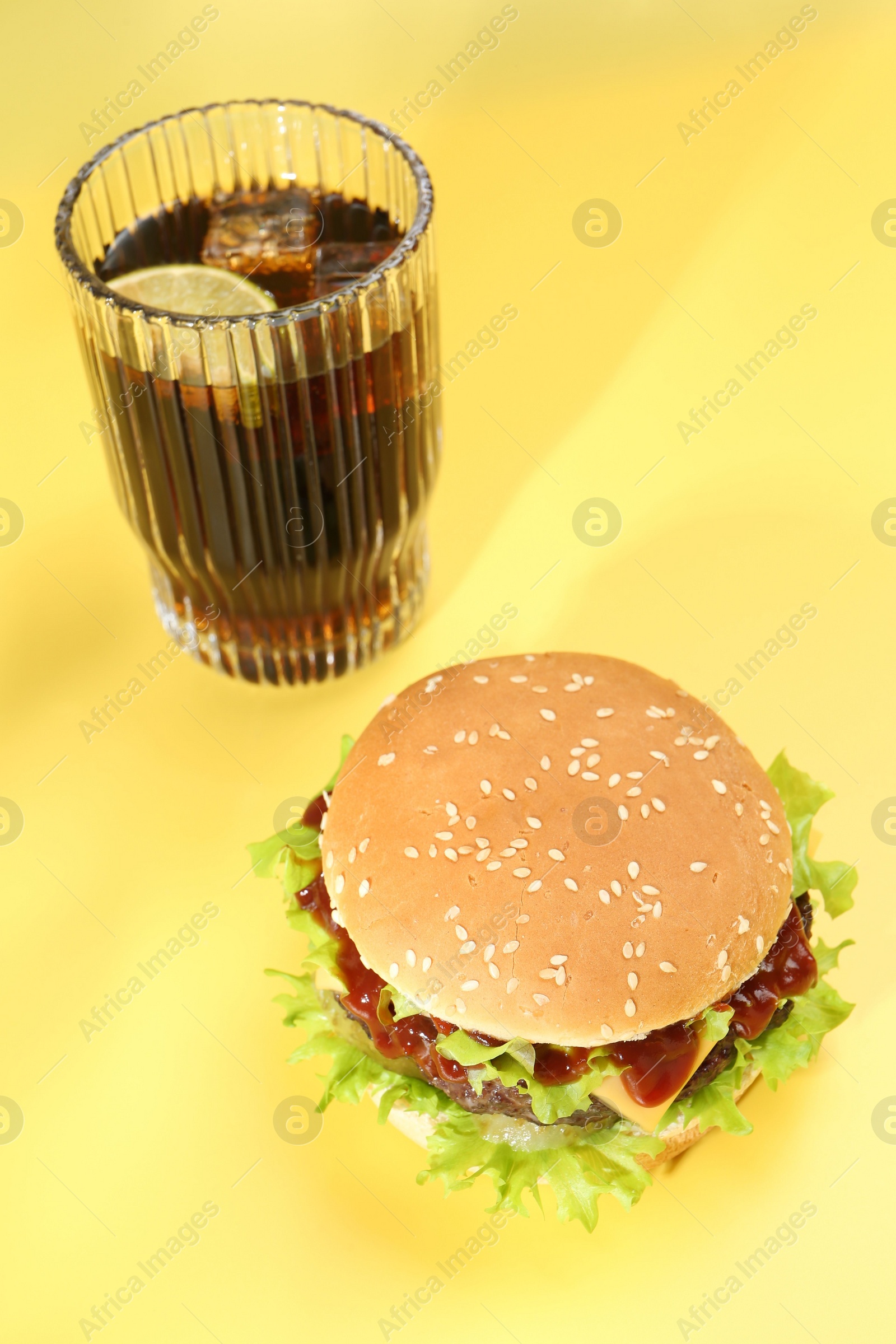 Photo of Burger with delicious patty and soda drink on yellow background