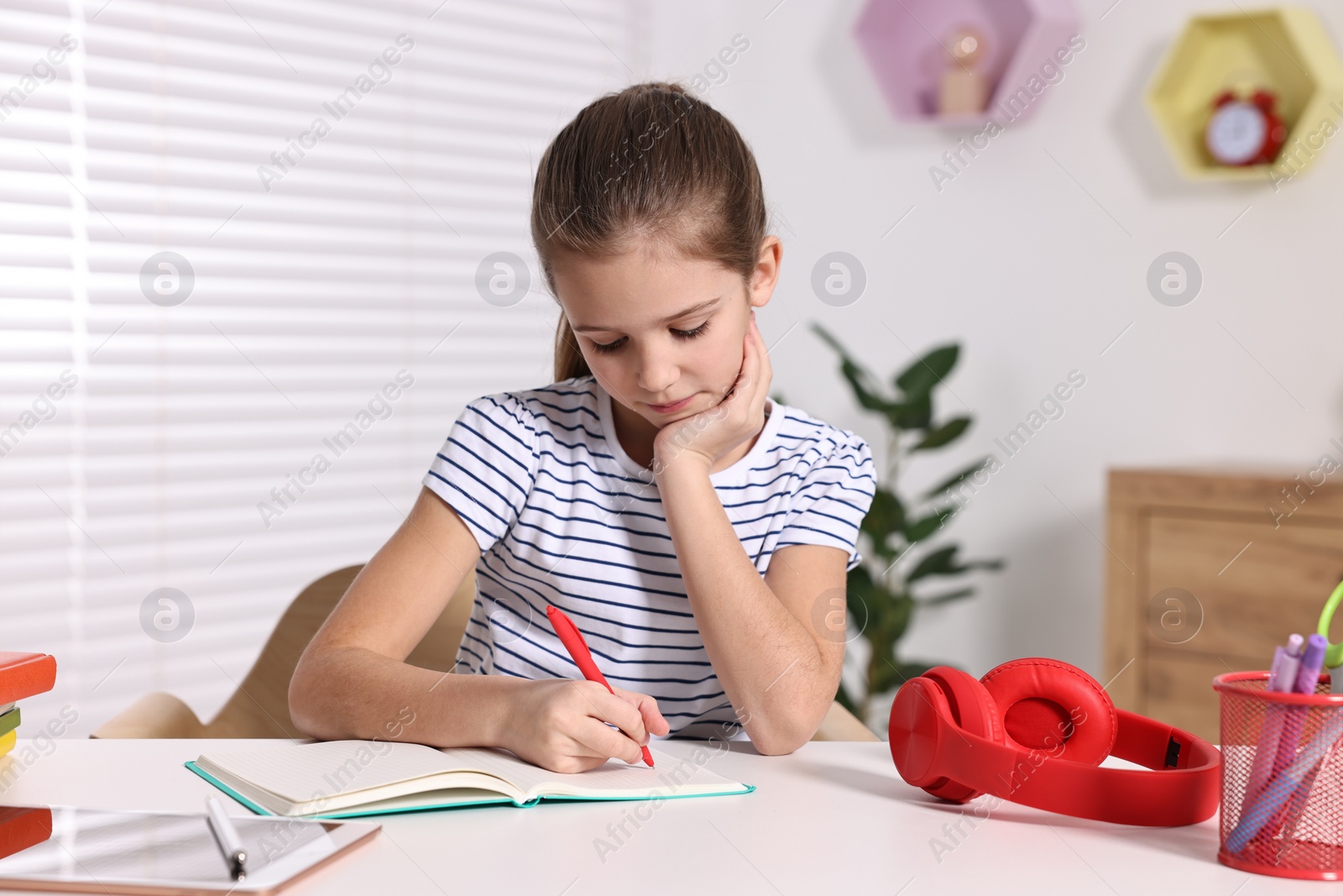 Photo of E-learning. Cute girl taking notes while studying online at table indoors