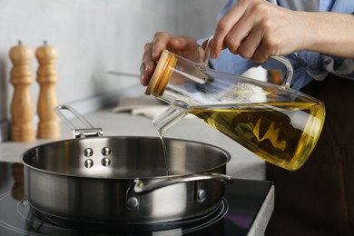 Photo of Vegetable fats. Woman pouring cooking oil into frying pan on stove in kitchen, closeup