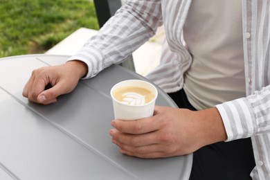 Photo of Coffee to go. Man with paper cup of drink at grey table outdoors, closeup