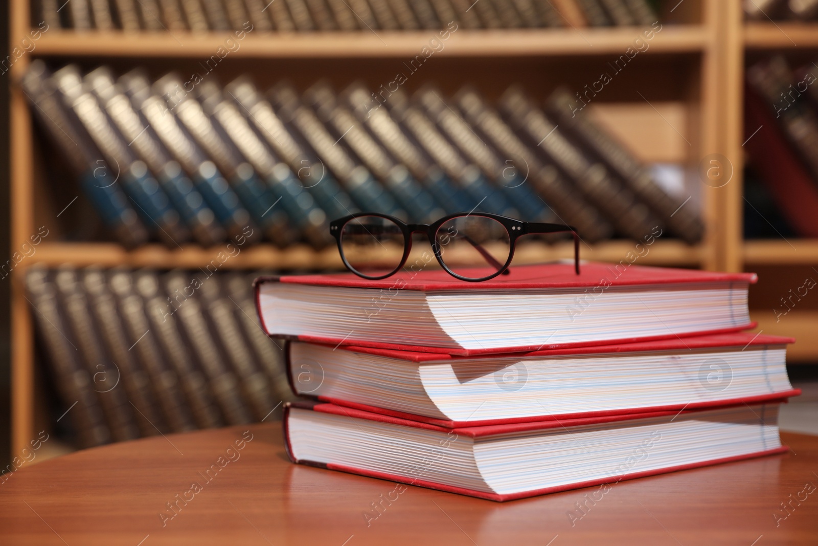 Photo of Stack of books and glasses on table in library. Space for text