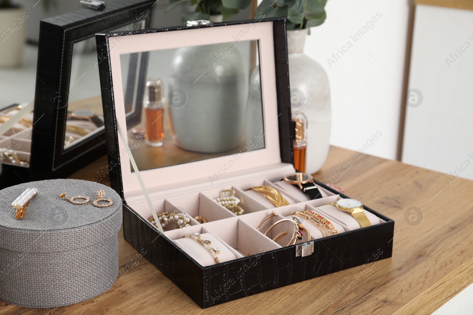 Photo of Elegant jewelry box with beautiful bijouterie and expensive wristwatches near luxury perfume on wooden table