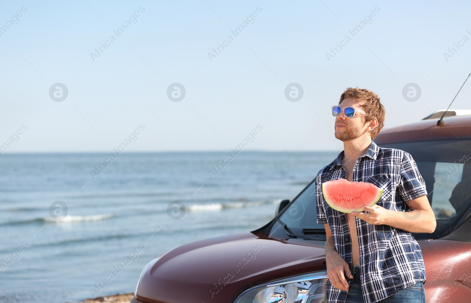 Photo of Young man with watermelon slice near car on beach. Space for text