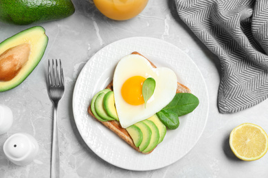 Photo of Tasty breakfast with heart shaped fried egg served on  grey table, flat lay