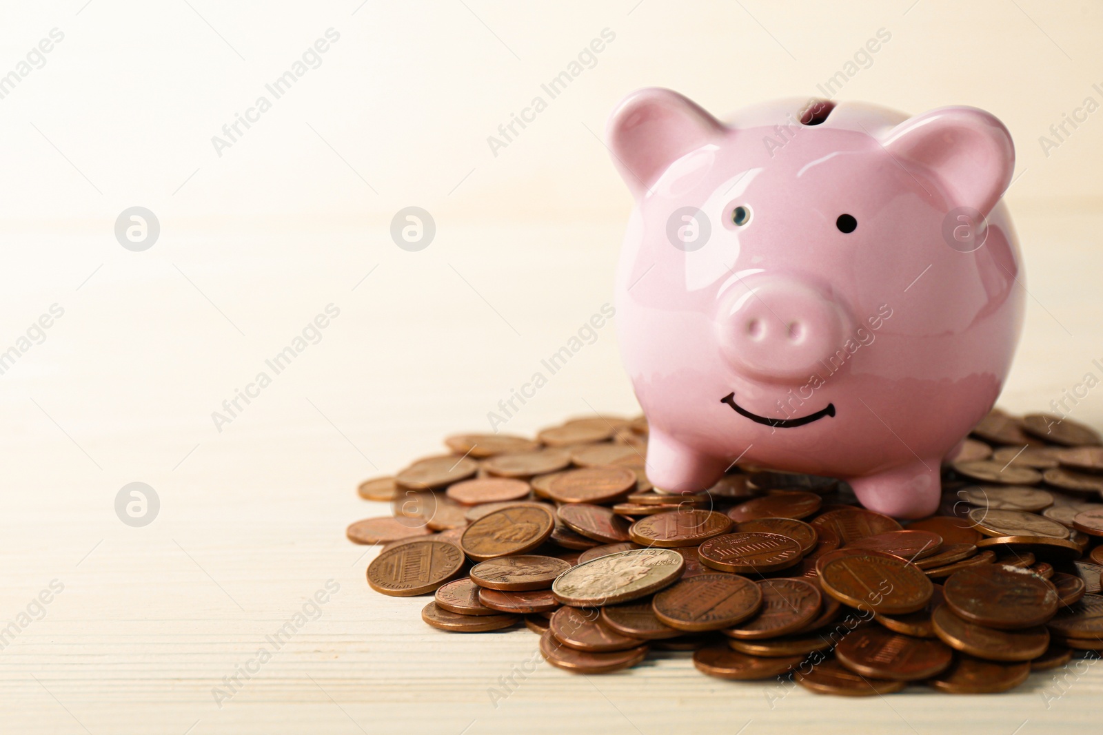 Photo of Ceramic piggy bank and coins on white wooden table, closeup. Space for text