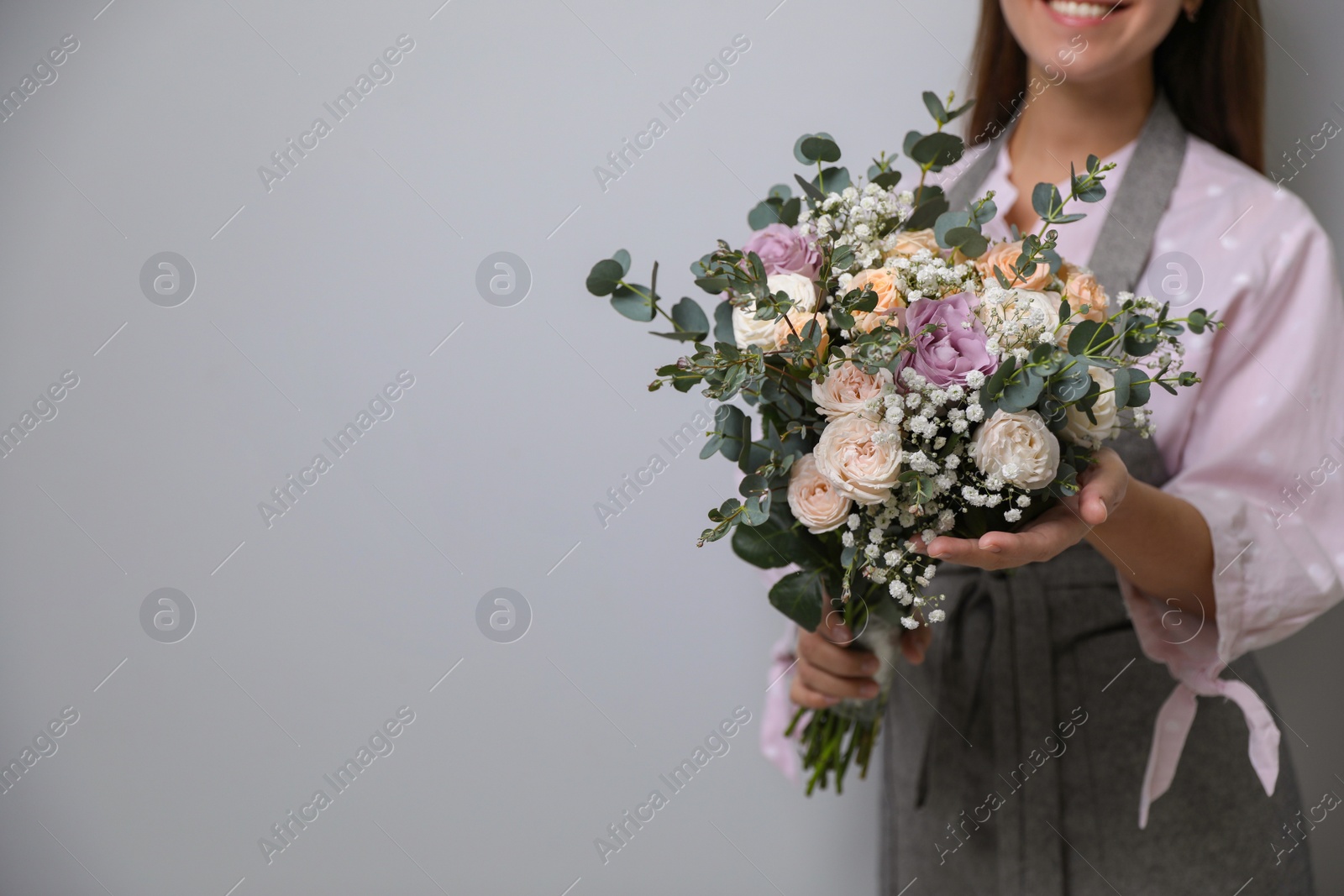 Photo of Florist holding beautiful wedding bouquet on light grey background, closeup. Space for text