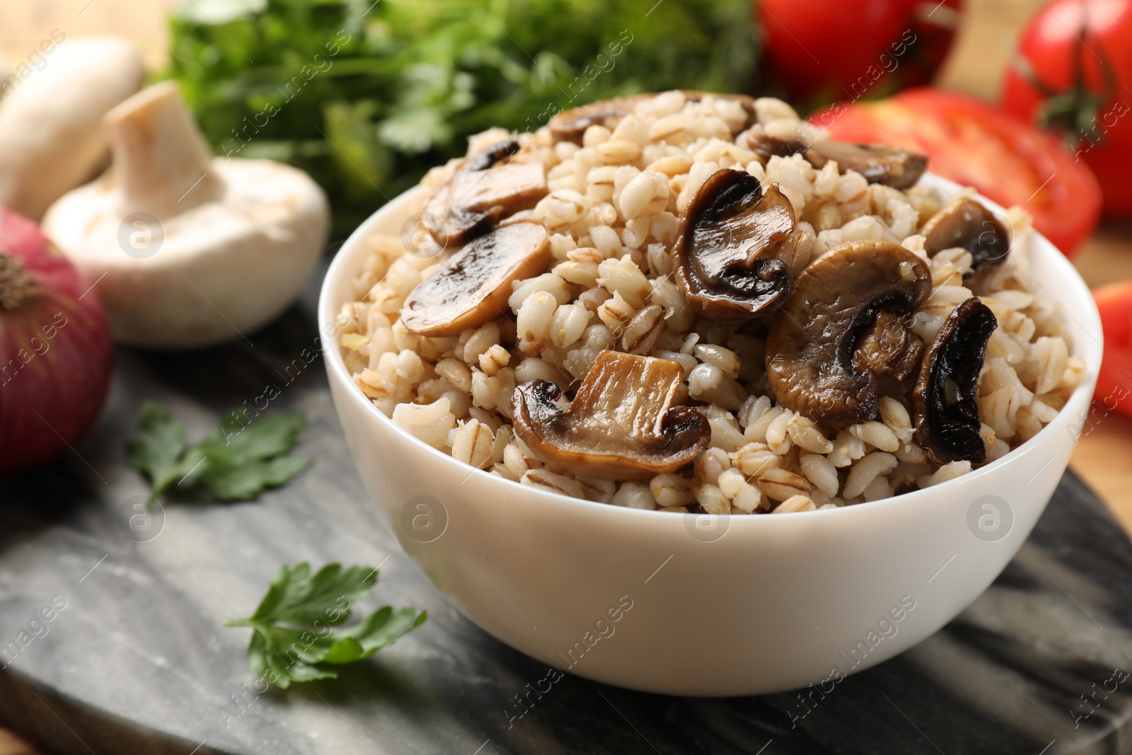 Photo of Delicious pearl barley with mushrooms in bowl on table, closeup