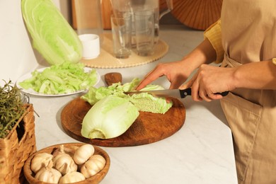 Photo of Woman cutting fresh chinese cabbage at kitchen table, closeup