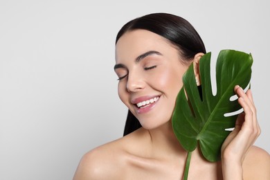 Woman holding leaf of monstera on light grey background, space for text. Spa treatment