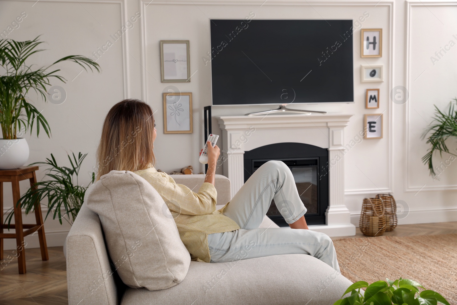 Photo of Young woman watching television at home. Living room interior with TV on fireplace