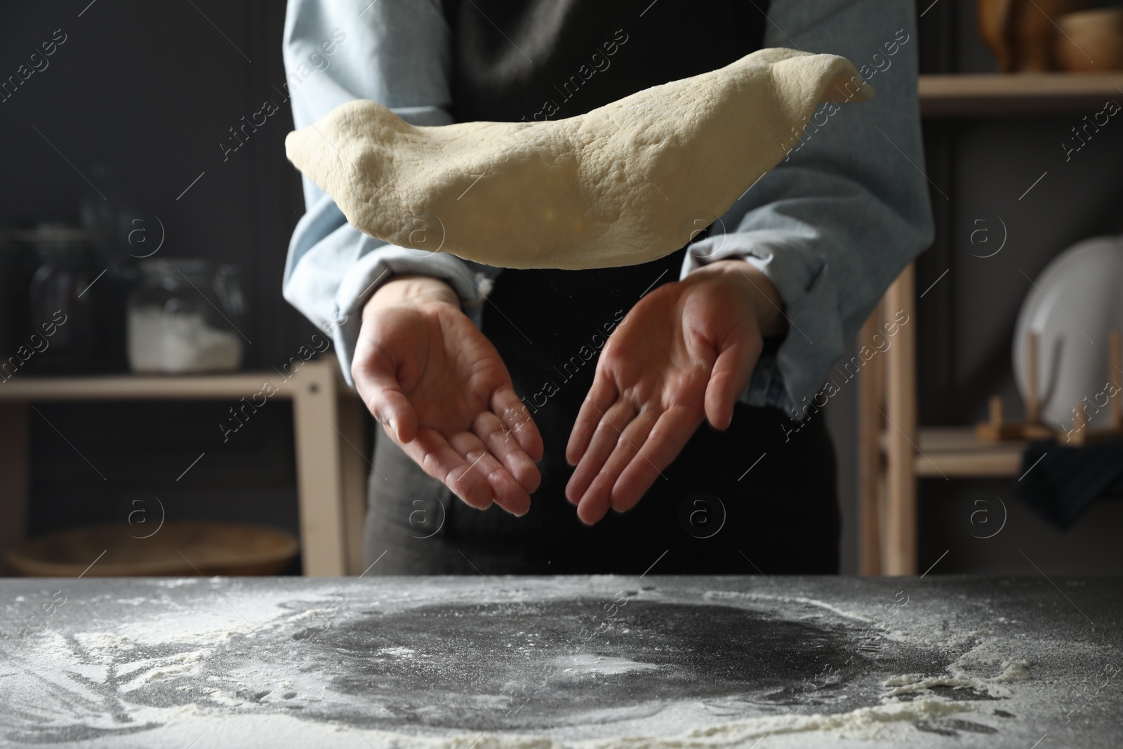 Photo of Woman tossing pizza dough at table in kitchen, closeup