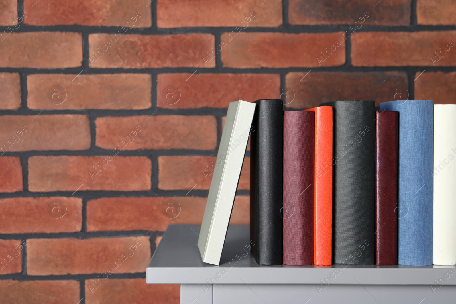 Photo of Many different hardcover books on grey table near brick wall. Space for text